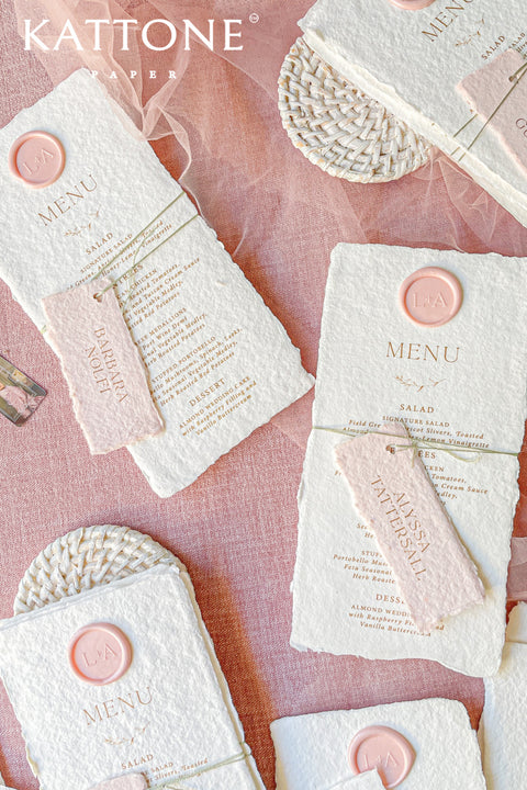 These handmade paper wedding menus capture the essence of romance and artisanal beauty. Crafted from 100% cotton rag paper, each menu features deckled edges, a luxurious tactile finish, and a timeless aesthetic that perfectly complements any elegant tablescape. The menus are adorned with a personalized wax seal and a custom name tag, adding a thoughtful, bespoke touch that enhances your guests’ dining experience.