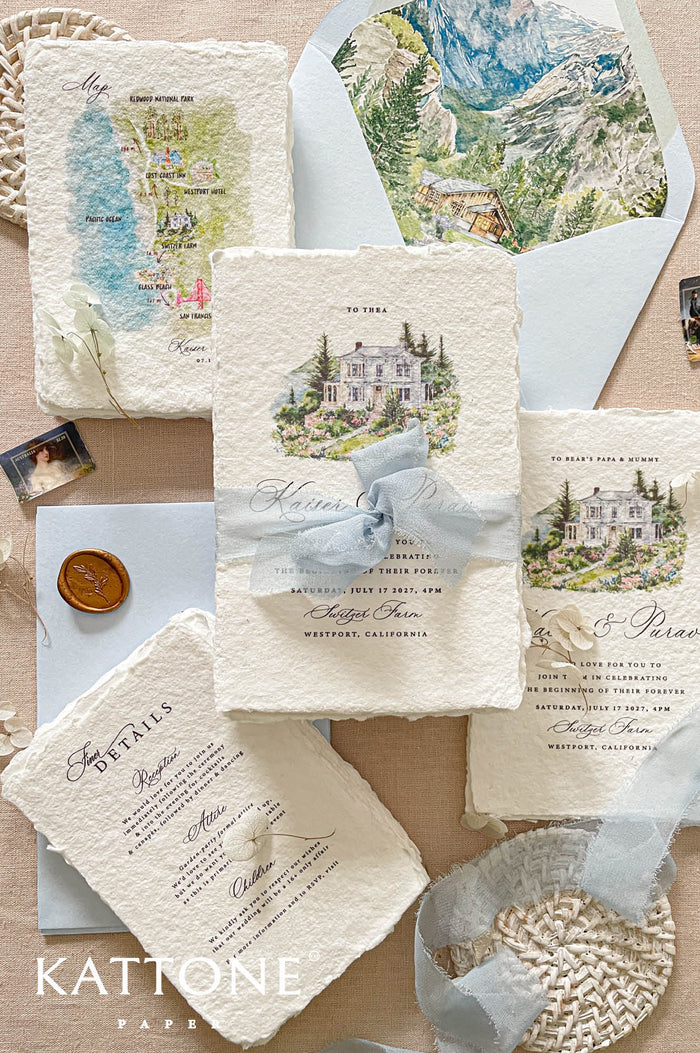 Luxury handmade paper wedding invitation suite featuring custom watercolor venue artwork, scenic envelope liners, watercolor map inserts, deckled edge cotton paper cards, and dusty blue chiffon ribbon styling.