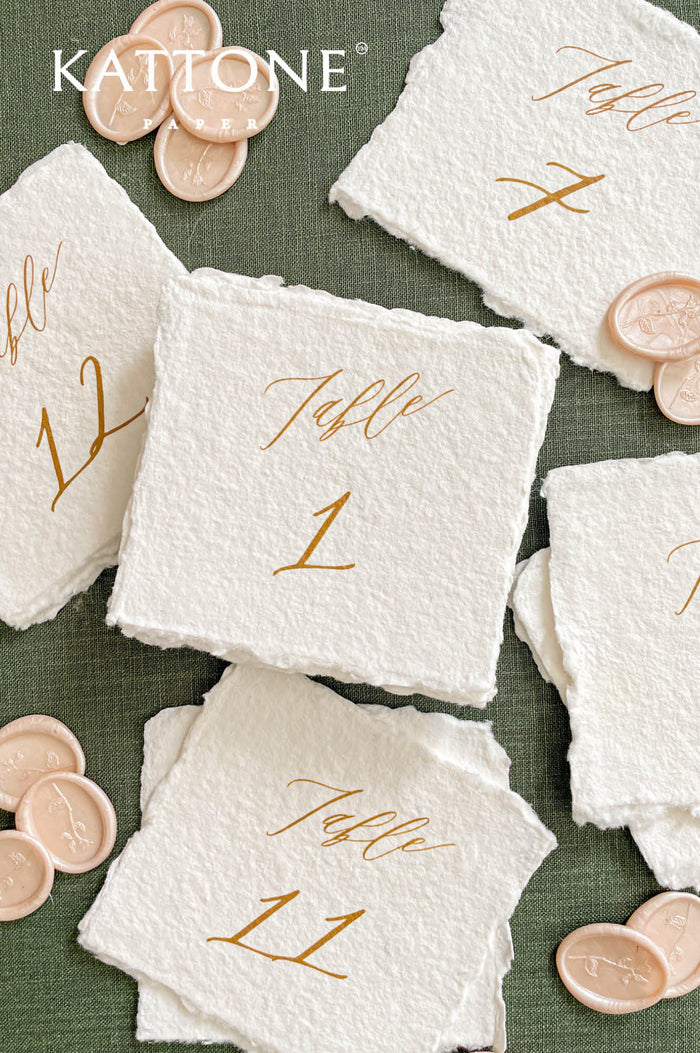 Assorted handmade paper table numbers with calligraphy script for elegant wedding tables.