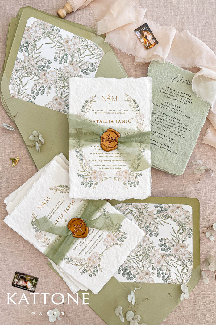 Luxury handmade cotton paper wedding invitation with deckled edges and botanical watercolor florals, styled with sage silk ribbon, wax seal and green envelopes with floral liners.