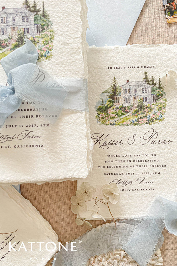 Premium handmade wedding invitation suite with custom watercolor venue illustrations, deckled edge cotton paper, scenic envelope liners, map inserts, and soft dusty blue accents for elegant destination weddings.