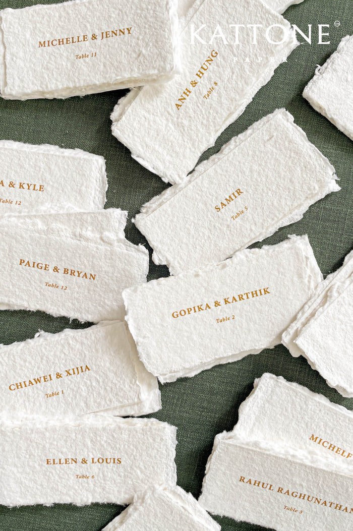 Handmade paper escort cards with deckled edges and gold guest names, luxury wedding seating cards on textured cotton paper.