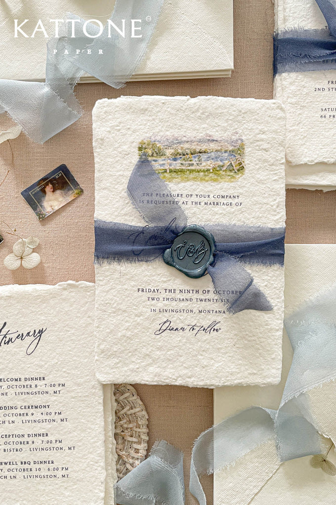 Premium handmade wedding invitation suite with watercolor artwork, deckled edge cotton paper, dusty blue chiffon ribbon, wax seal accents, and soft neutral styling for elegant weddings.