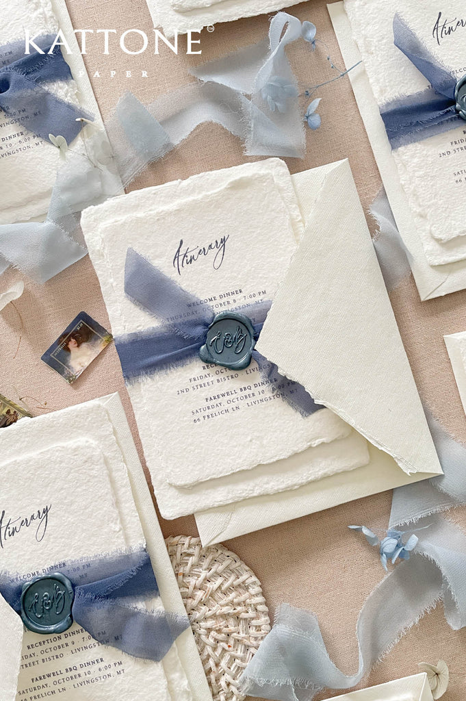 Romantic flat lay of luxury wedding stationery showcasing handmade paper invitation cards, itinerary inserts, chiffon ribbon styling, wax seal details, and coordinated ivory envelopes.