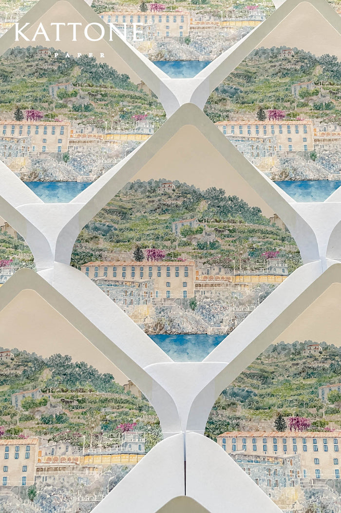 Luxury ivory wedding envelopes with custom watercolor coastal liners featuring romantic Mediterranean landscape artwork in soft blue and green tones.