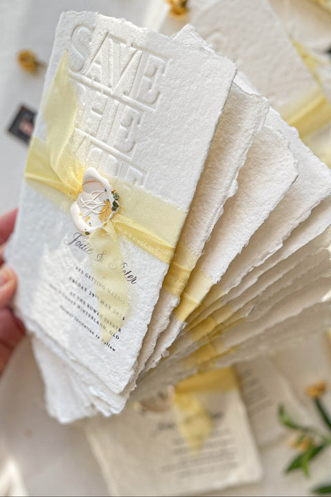 Announce your wedding with refined elegance through our embossed handmade paper Save the Date cards, crafted on luxury 100% cotton handmade paper with soft deckled edges. The embossed impression adds texture and sophistication, while each card is wrapped in a buttery yellow silk ribbon and sealed with a hand-pressed wax seal, creating a timeless and romantic presentation.