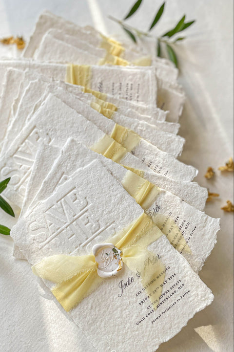 Announce your wedding with refined elegance through our embossed handmade paper Save the Date cards, crafted on luxury 100% cotton handmade paper with soft deckled edges. The embossed impression adds texture and sophistication, while each card is wrapped in a buttery yellow silk ribbon and sealed with a hand-pressed wax seal, creating a timeless and romantic presentation.