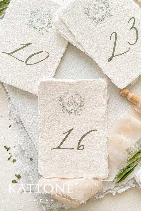 Watercolor greenery and handmade deckle-edge cotton paper create a naturally elegant table number design that brings soft, organic beauty to your wedding décor. The delicate botanical wreath and refined numeral style add a fine-art, timeless touch, making each card feel both romantic and elevated. Perfect for garden weddings, outdoor celebrations, and nature-inspired themes, this design blends airy watercolor tones with luxurious craftsmanship.
