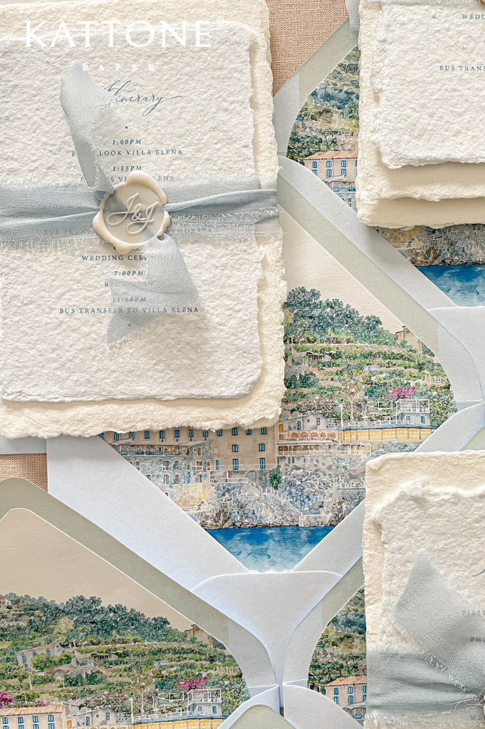 Soft blue wedding envelopes with custom watercolor coastal landscape liners featuring detailed scenic artwork inspired by the Amalfi Coast.