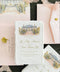 Close-up of an elegant ivory handmade paper wedding save the date card featuring a custom watercolor illustration of a glass conservatory with garden steps, vintage lampposts, and lush greenery. Gold calligraphy and classic typography complement the textured deckled paper, styled with blush pink envelopes, matching watercolor liners, and delicate botanical accents.