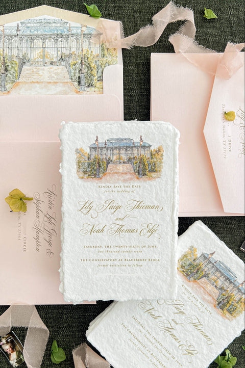 Close-up of an elegant ivory handmade paper wedding save the date card featuring a custom watercolor illustration of a glass conservatory with garden steps, vintage lampposts, and lush greenery. Gold calligraphy and classic typography complement the textured deckled paper, styled with blush pink envelopes, matching watercolor liners, and delicate botanical accents.