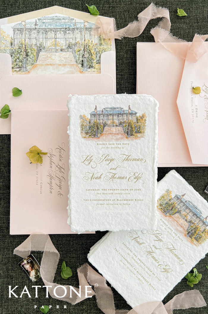 Close-up of an elegant ivory handmade paper wedding save the date card featuring a custom watercolor illustration of a glass conservatory with garden steps, vintage lampposts, and lush greenery. Gold calligraphy and classic typography complement the textured deckled paper, styled with blush pink envelopes, matching watercolor liners, and delicate botanical accents.