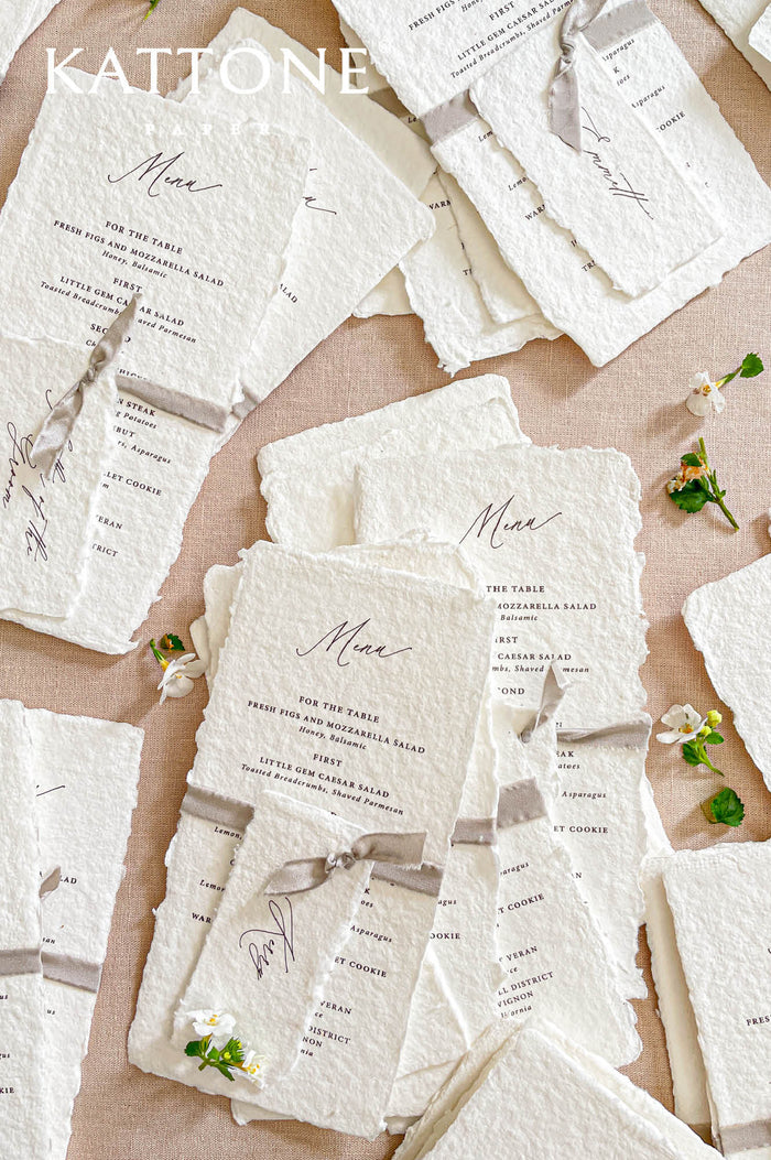 Handmade paper wedding menu with deckled edges, minimalist typography, ribbon tie detail, fine art reception stationery flat lay.