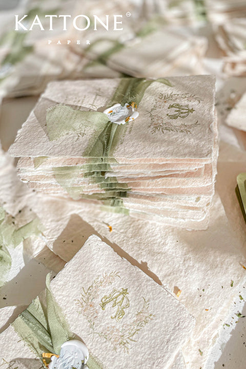 Soft, organic, and undeniably romantic - this colored handmade paper wedding invitation suite beautifully captures the essence of nature-inspired elegance. Printed on luxury blush-toned deckled-edge cotton paper, each piece is a work of art, blending timeless craftsmanship with delicate botanical elements and refined greenery details. At its heart lies a custom hand-drawn monogram, surrounded by soft watercolor foliage - a symbol of the couple’s unity and natural grace. 