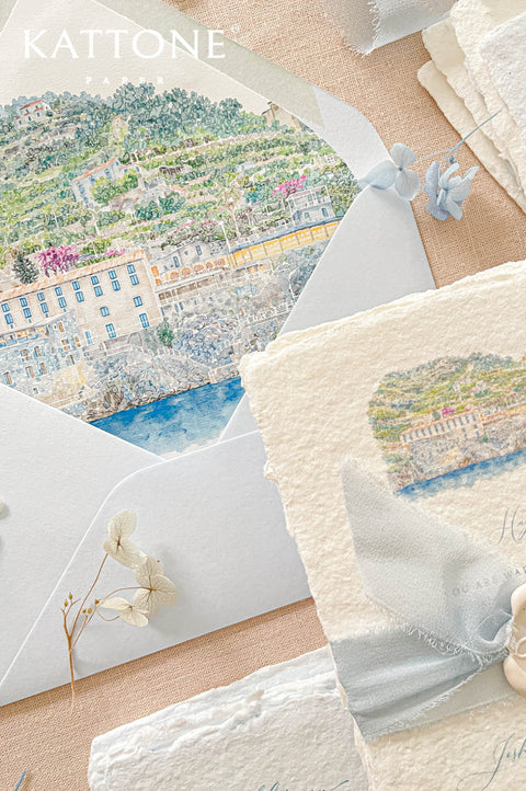 Wedding envelopes arranged in a flat lay showcasing custom watercolor envelope liners with romantic coastal landscape artwork.