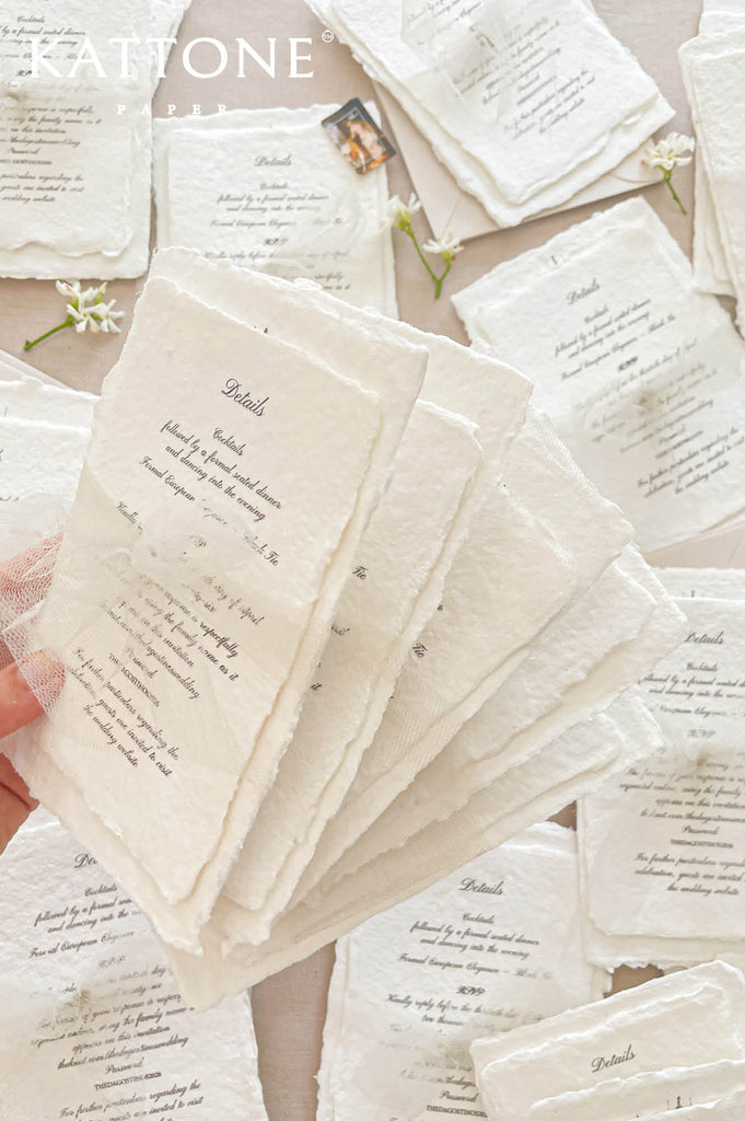 Close up of textured handmade cotton paper invitation showing organic deckled edges, fine architectural line drawing and elegant typography.
