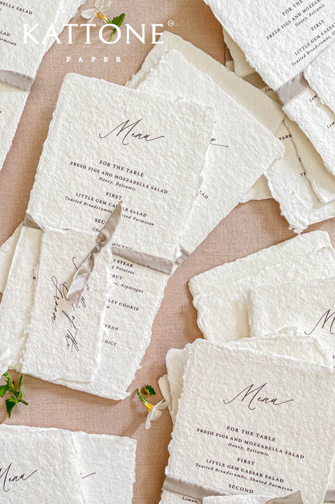 Stacked handmade paper wedding menus with deckled edges and ribbon ties for elegant reception tables.