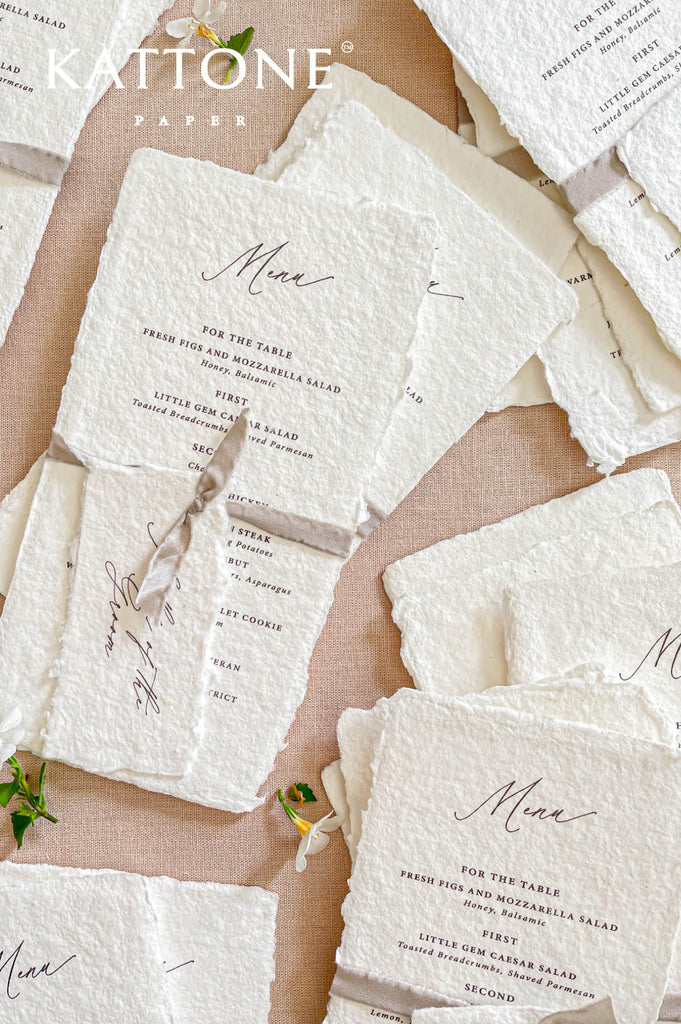 Stacked handmade paper wedding menus with deckled edges and ribbon ties for elegant reception tables.