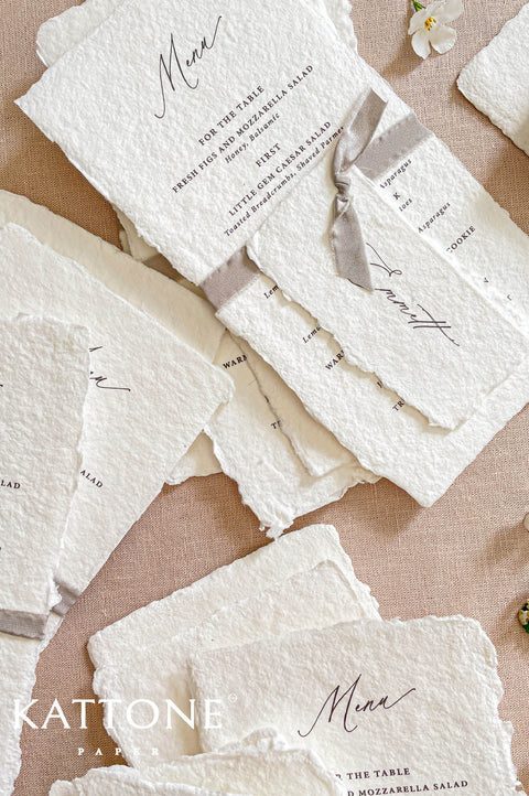 Close-up of handmade cotton paper wedding menu with organic deckled edges and soft textured surface.
