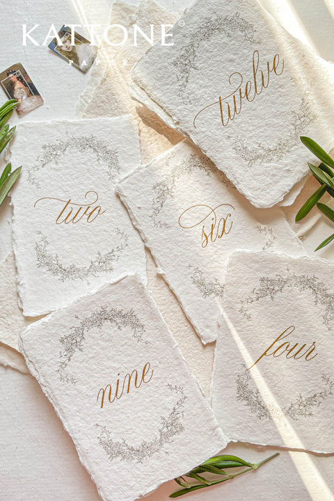 Soft floral wreaths and handcrafted deckle-edge cotton paper come together to create table numbers with a refined, organic aesthetic. The flowing gold script adds warmth and sophistication, while the botanical detailing enhances the romantic, fine-art charm. Perfect for garden weddings, outdoor celebrations, and naturally inspired décor, this design brings a delicate, timeless touch to every table.