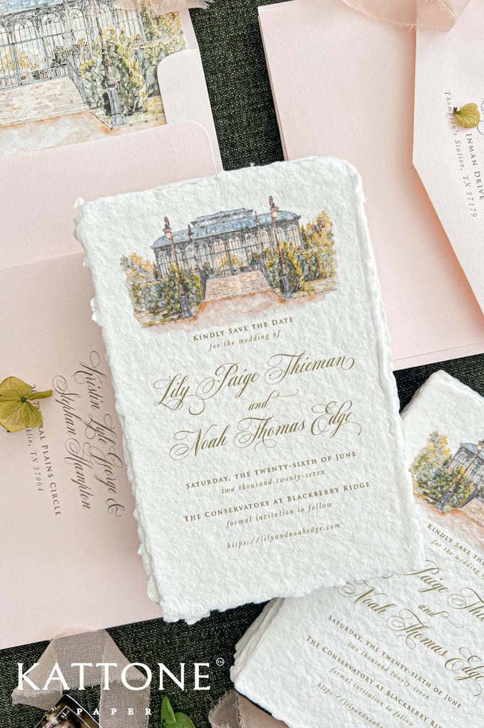 Overhead detail of an ivory handmade paper save the date card featuring watercolor artwork of a glass conservatory and personalized gold calligraphy. Surrounded by blush pink wedding envelopes with illustrated liners, coordinating address printing, soft blush ribbon, and delicate green floral accents, highlighting the textured deckled edges and romantic botanical wedding stationery design.