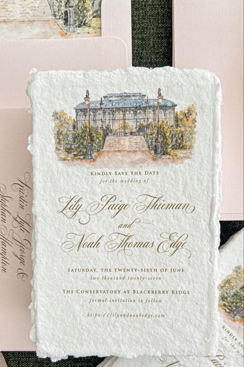 Close-up of an elegant ivory handmade paper wedding save the date card featuring a custom watercolor illustration of a glass conservatory with garden steps, vintage lampposts, and lush greenery. Gold calligraphy and classic typography complement the textured deckled paper, styled with blush pink envelopes, matching watercolor liners, and delicate botanical accents.