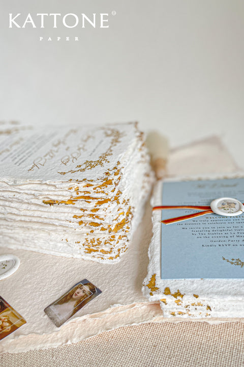 Invite your guests to your special day with the artful beauty of these exquisite handmade paper wedding invites. Perfect for a garden wedding, these invitations feature a delicate golden leaf addition, providing a touch of understated elegance and luxurious shimmer. The tactile and organic feel of the deckle edge paper creates a truly memorable keepsake, setting a romantic and refined tone for your celebration.