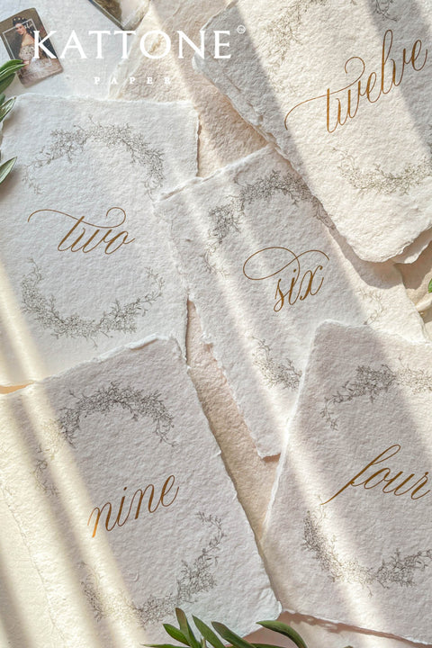 Soft floral wreaths and handcrafted deckle-edge cotton paper come together to create table numbers with a refined, organic aesthetic. The flowing gold script adds warmth and sophistication, while the botanical detailing enhances the romantic, fine-art charm. Perfect for garden weddings, outdoor celebrations, and naturally inspired décor, this design brings a delicate, timeless touch to every table.