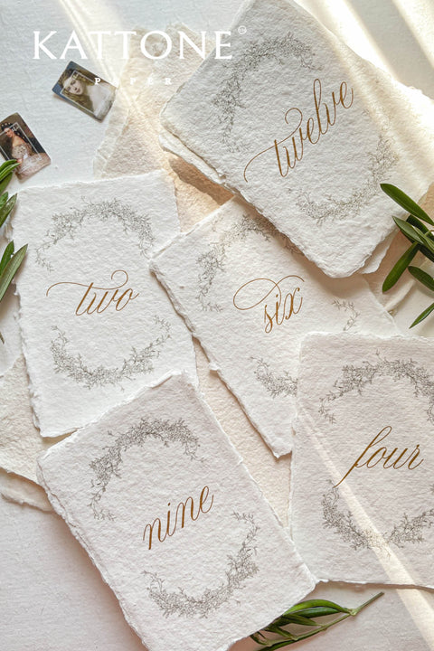Soft floral wreaths and handcrafted deckle-edge cotton paper come together to create table numbers with a refined, organic aesthetic. The flowing gold script adds warmth and sophistication, while the botanical detailing enhances the romantic, fine-art charm. Perfect for garden weddings, outdoor celebrations, and naturally inspired décor, this design brings a delicate, timeless touch to every table.