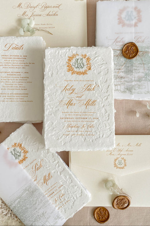 Luxury embossed handmade paper wedding invitation suite featuring deckled edge cotton paper, raised floral embossing, gold typography, custom monogram crest, vellum cover with wax seal, and coordinated ivory envelopes.