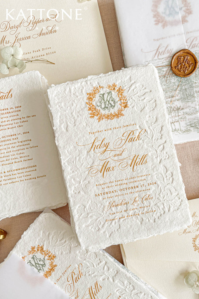 Elegant embossed handmade cotton paper wedding invitation with deckled edges, intricate raised floral embossing, gold typography, custom botanical crest monogram, and a soft vellum cover for layered styling.