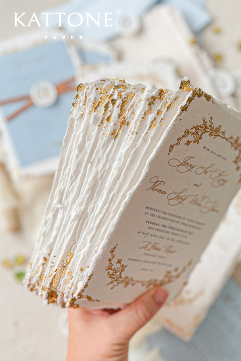 Invite your guests to your special day with the artful beauty of these exquisite handmade paper wedding invites. Perfect for a garden wedding, these invitations feature a delicate golden leaf addition, providing a touch of understated elegance and luxurious shimmer. The tactile and organic feel of the deckle edge paper creates a truly memorable keepsake, setting a romantic and refined tone for your celebration.