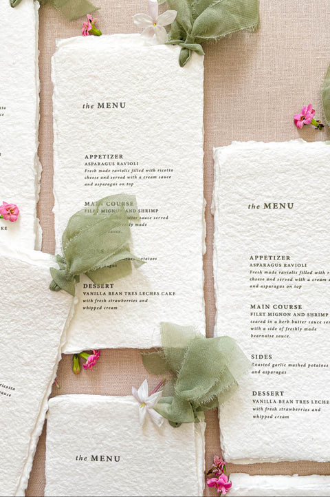 Fine art wedding menus on handmade paper styled with sage silk ribbon, neutral linens, and botanical details.