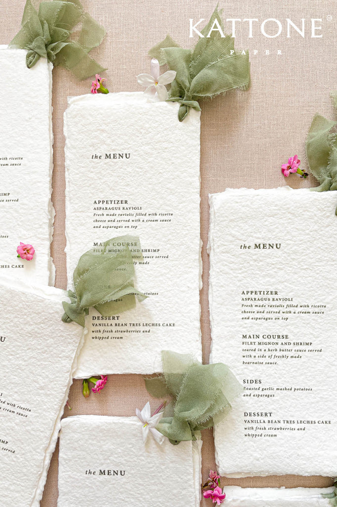 Fine art wedding menus on handmade paper styled with sage silk ribbon, neutral linens, and botanical details.