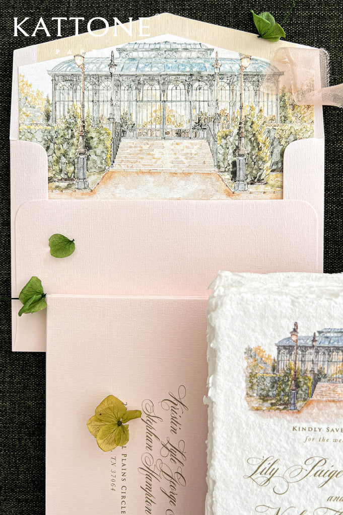 Detailed close-up of a blush wedding envelope featuring a custom watercolor conservatory liner with soft blue architectural details, a glass roof, stone steps, ornate lampposts, and sage green garden foliage. Styled alongside a matching textured pink envelope with elegant personalized guest address printing, a white deckle-edge save the date card, and soft blush silk ribbon.