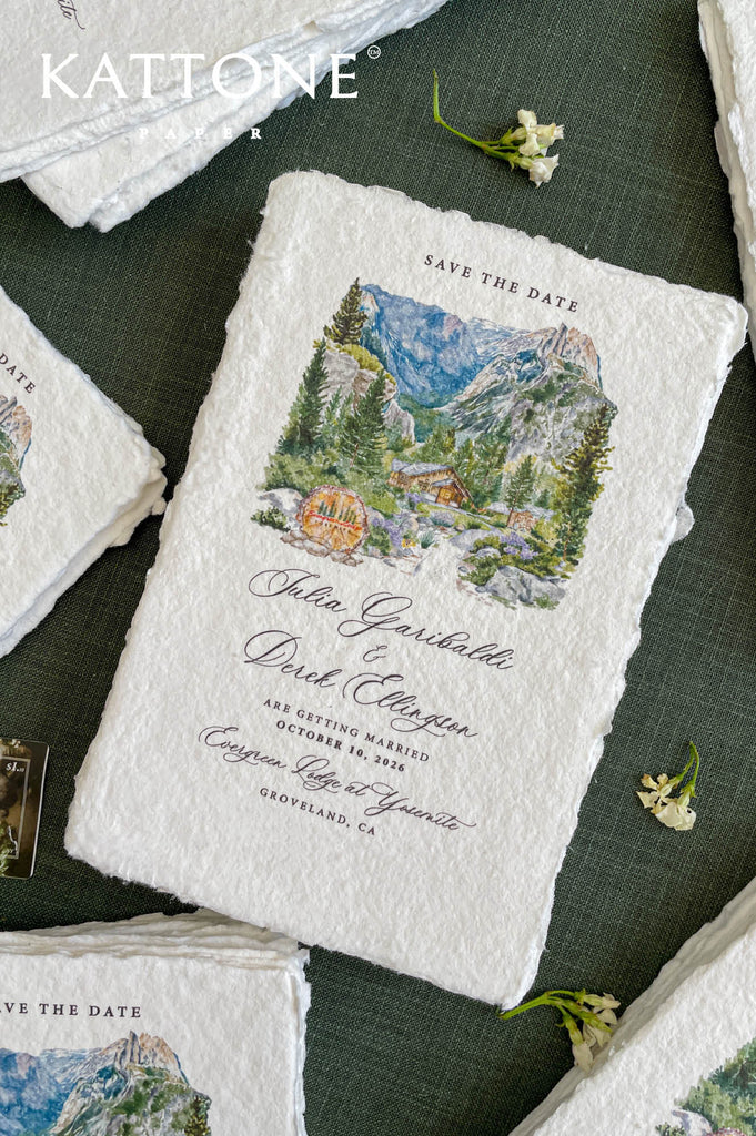 Close-up of handmade paper save the date card featuring a watercolor mountain wedding venue illustration.