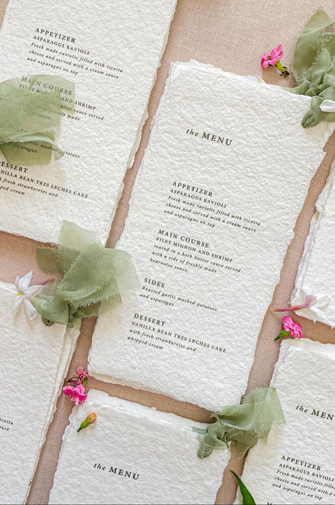 Close-up of handmade cotton paper wedding menu with organic deckled edges and softly textured surface.
