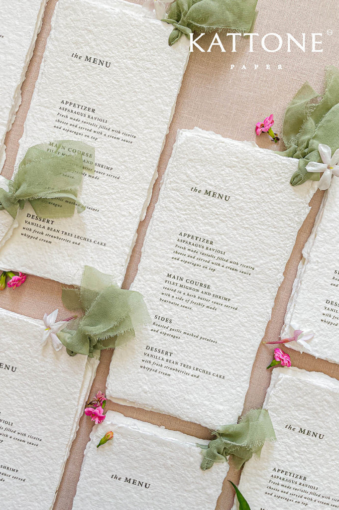 Close-up of handmade cotton paper wedding menu with organic deckled edges and softly textured surface.