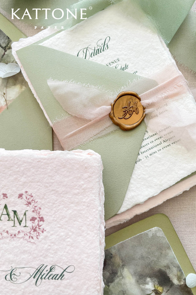 Premium colored handmade paper wedding invitation suite with floral monogram artwork, blush cotton paper, watercolor floral details, and elegant calligraphy for romantic luxury weddings.