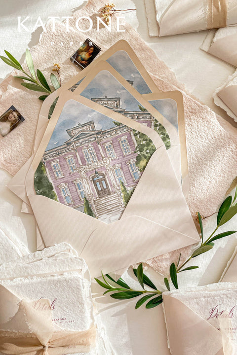 Wedding envelopes with watercolor venue envelope liners styled with handmade paper, soft ribbon, and fine art wedding stationery details.