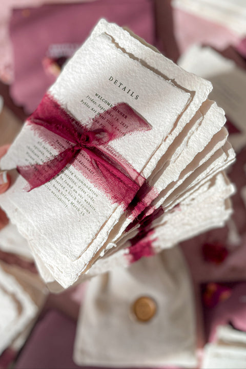 Romantic, rich, and full of timeless charm - this handmade paper wedding invitation suite is the perfect harmony of texture, elegance, and deep color. Each invitation is printed on luxurious cotton handmade paper with naturally deckled edges, exuding an organic and artisanal feel that makes every piece truly one of a kind. The suite is beautifully complemented by deep burgundy envelopes and tied with flowing silk chiffon ribbons in wine red, adding warmth, passion, and sophistication.