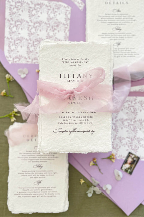 Luxury handmade cotton paper wedding invitation with deckled edges wrapped in blush silk ribbon, styled with lavender envelopes and botanical envelope liners.