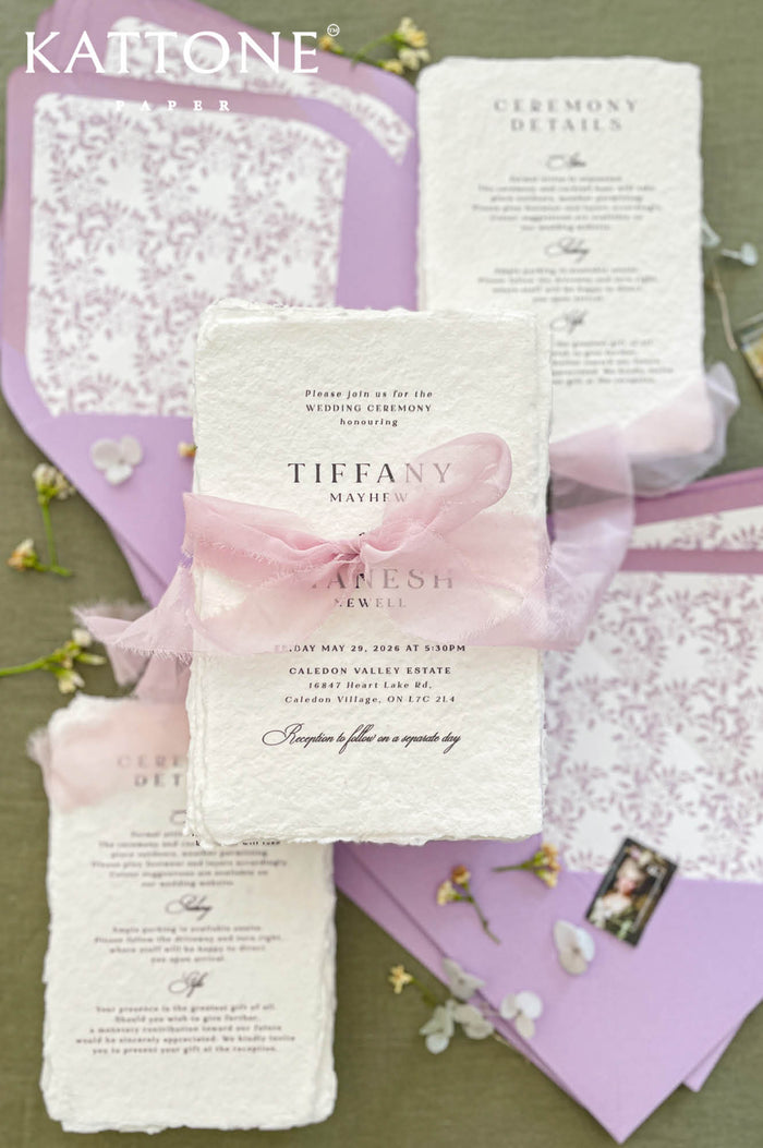 Luxury handmade cotton paper wedding invitation with deckled edges wrapped in blush silk ribbon, styled with lavender envelopes and botanical envelope liners.