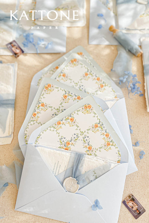 Light blue wedding envelopes with watercolor floral envelope liners styled with silk ribbon, wax seal, and fine art wedding stationery details.