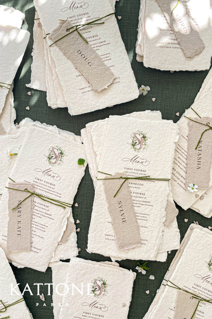 Stacked handmade paper wedding menus with watercolor monogram and deckled edges for elegant table settings.