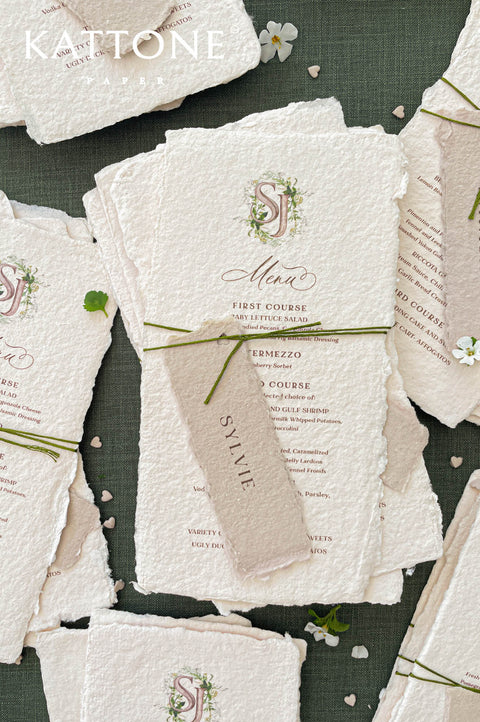 Handmade paper wedding menu with deckled edges and custom watercolor monogram, fine art reception stationery flat lay.