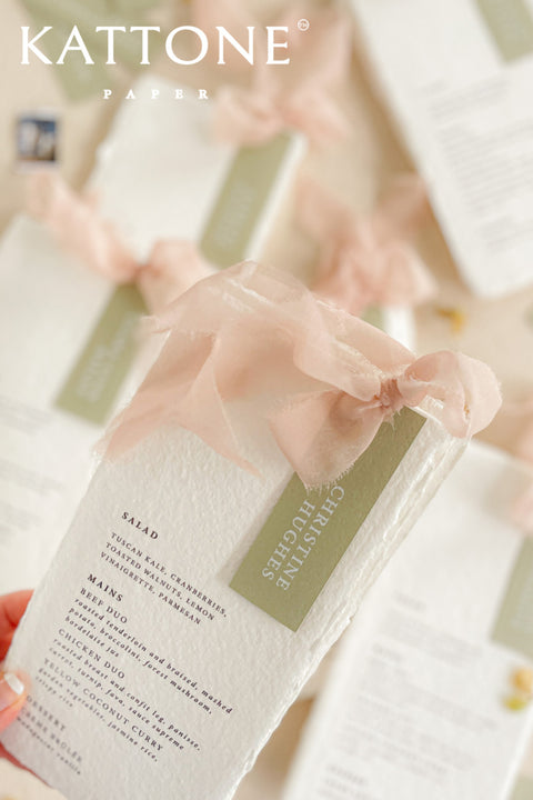 Elevate your tablescape with our handmade paper wedding menus with personalized name tags, crafted from soft cotton paper with naturally deckled edges. Each menu exudes fine-art elegance, featuring delicate typography, custom color tags, and flowing chiffon ribbons - blending romance, craftsmanship, and sophistication. Perfect for luxury, garden, and destination weddings, these menus double as keepsake place cards.