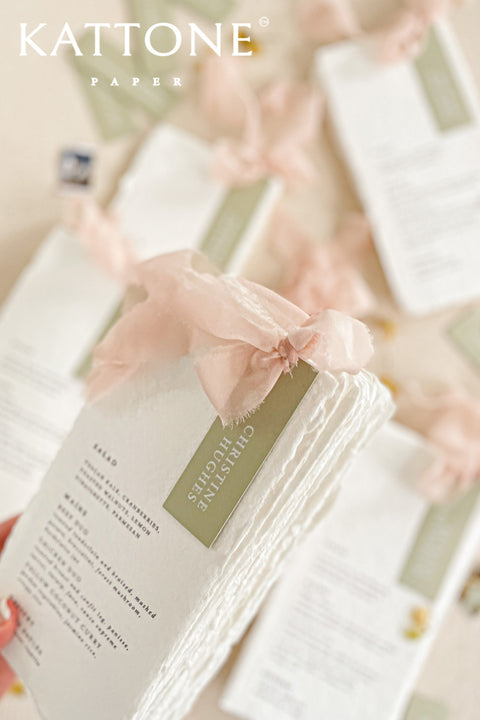 Elevate your tablescape with our handmade paper wedding menus with personalized name tags, crafted from soft cotton paper with naturally deckled edges. Each menu exudes fine-art elegance, featuring delicate typography, custom color tags, and flowing chiffon ribbons - blending romance, craftsmanship, and sophistication. Perfect for luxury, garden, and destination weddings, these menus double as keepsake place cards.