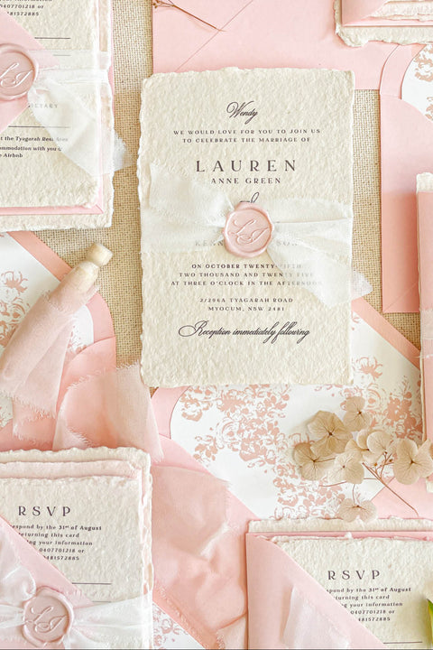 This handmade paper wedding invitation suite exudes timeless elegance with a touch of modern artistry. Crafted on luxury cotton paper with deckled edges, each invitation tells a story of care and craftsmanship. The delicate texture pairs beautifully with blush and ivory tones, creating a look that feels both classic and ethereal. Every detail is completed with a wax seal monogram, adding a touch of old-world refinement.