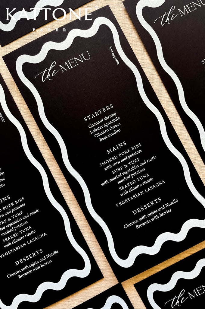Flat lay of modern black wedding menus arranged for an elegant rehearsal dinner tablescape.